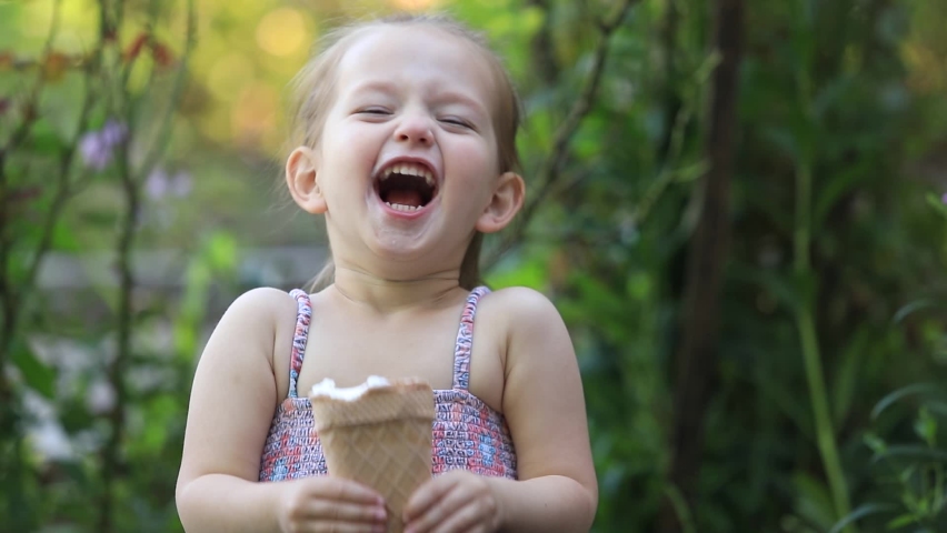 Portrait of a little beautiful girl eating ice cream and smiling outdoors shot in slow motion | Shutterstock HD Video #1060307750