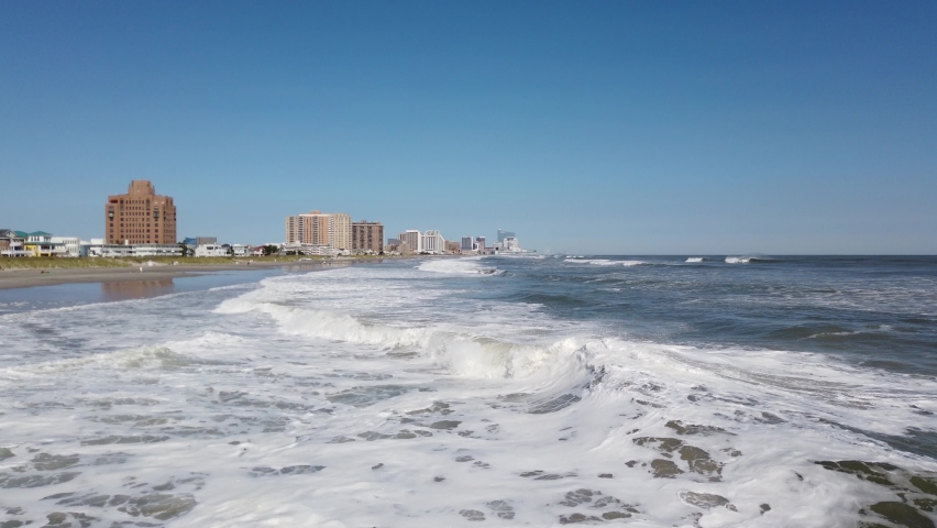 View along an Atlantic Ocean coastline with waves breaking as they approach the shore. Atlantic City is seen in the distance.