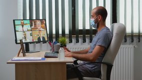 Freelancer making a video conference with face mask in modern office room. Entrepreneur working in new normal workplace having online meeting, webinar with remotely team using internet technology