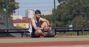 Young bearded guy texting on smartphone, waiting for friends at outdoor basketball court