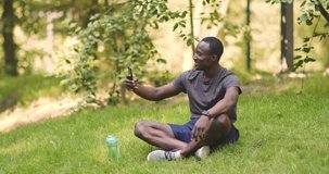 Modern communication. Cheerful african american guy talking on mobile phone, sitting on grass in park