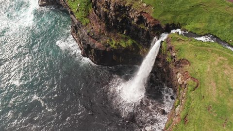 Stunning waterfall splashing from cliff aerial view. Mulafossur waterfall near Gasadalur Village at Faroe Islands. Overhead aerial establishing shot, daylight,cloudy weather