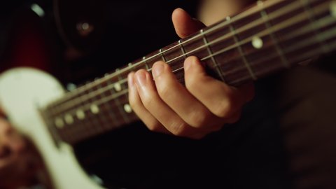 Guitarist hand pinching chords on electric guitar indoor. Unrecognizable person playing rock in recording studio. Unknown musician holding fretboard in repetition hall.