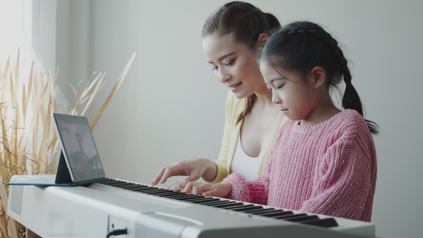 Mother Asian is teaching daughter to play an electric piano in house. Family activities that happy together. Online music school business. Concept video conference Royalty-Free Stock Footage #1060312880