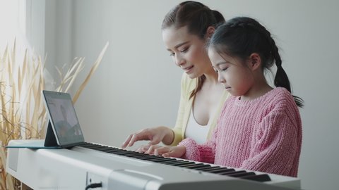 Mother Asian is teaching daughter to play an electric piano in house. Family activities that happy together. Online music school business. Concept video conference