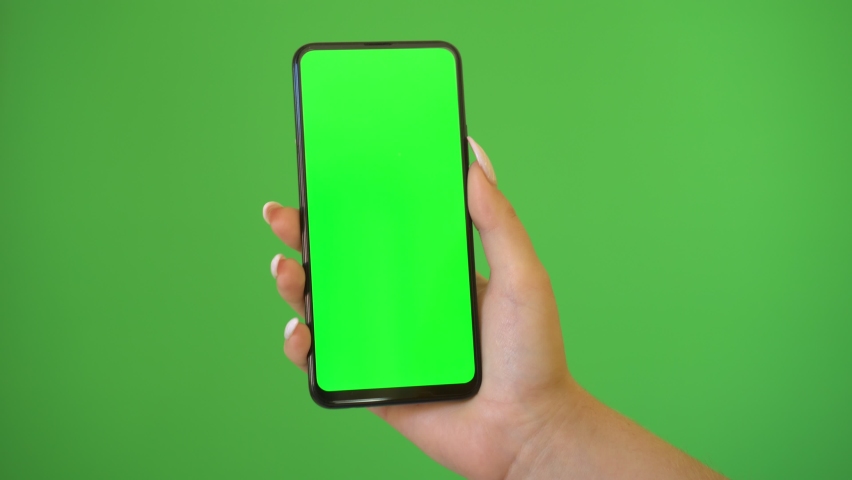 Woman hand holds a smartphone with greeen screen over a green background. | Shutterstock HD Video #1060313897