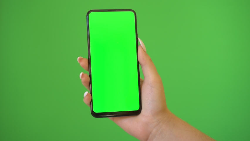 Woman hand holds a smartphone with greeen screen over a green background. | Shutterstock HD Video #1060313981