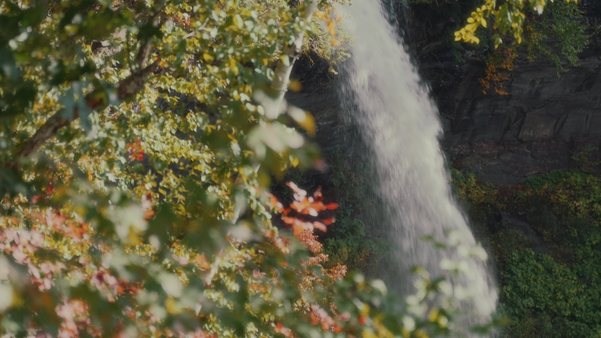 The magnificent Kaaterskill falls in upstate NY in fall through leaves blowing in the wind. 4k UHD