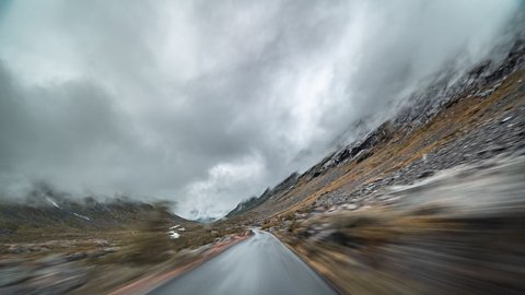 A drive on the Gamle Strynefjellsvegen, Norway. Thick white-gray clouds hanging above. Harsh tundra landscape is on the both sides of the road.
