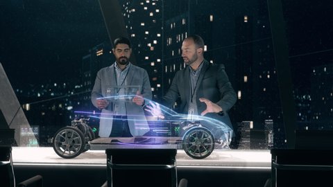 Mockup of Electric Vehicle: Automotive engineers working on design of Detailed Electric Car Chassis using futuristic transparent screens and AR Holographic Surface High Tech Table. High-tech facility 