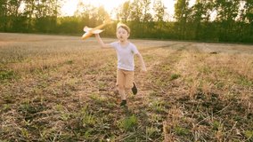 Happy child runs with a toy airplane on a sunset background over a field. The concept of a happy family. Childhood dreams.