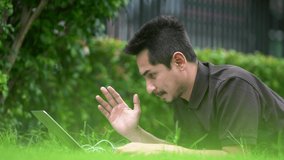 Asian young man using his laptop on a lawn.