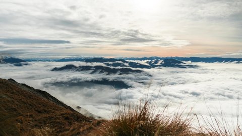 Time lapse: picturesque Wanaka colorful sunrise above thick opaque stratus billowing and rolling clouds blanketing Roys Peak mountain valley landscape, New Zealand