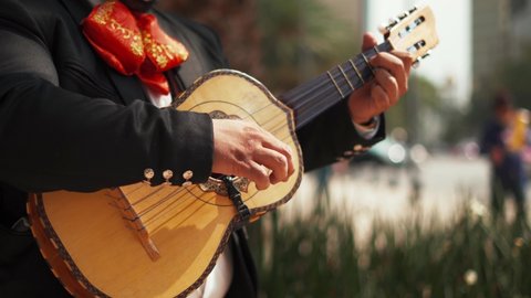 4k Video of a mariachi playing a five strings instrument called vihuela while a blurry street as the background