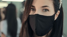 Green eyed female beautician wearing black protective mask stands near large mirror in professional cosmetic salon closeup
