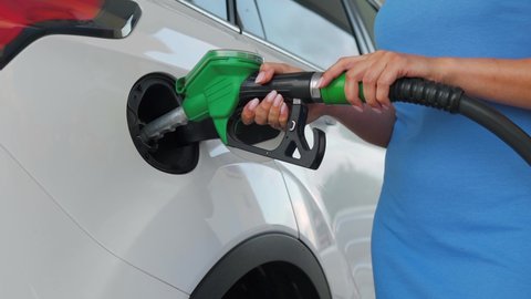 Woman inserts a fuel gun in a gas tank to refuel a car