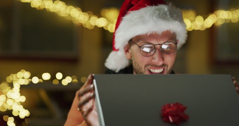 Authentic shot of happy young man is opening his Christmas present box is excited and surprised with received gift. Concept: winter holidays, tradition, surprise, e-commerce