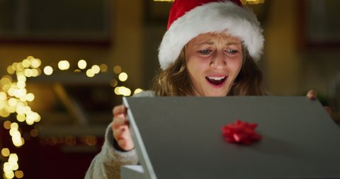 Authentic shot of happy young woman is opening her Christmas present box is excited and surprised with received gift. Concept: winter holidays, tradition, surprise, e-commerce