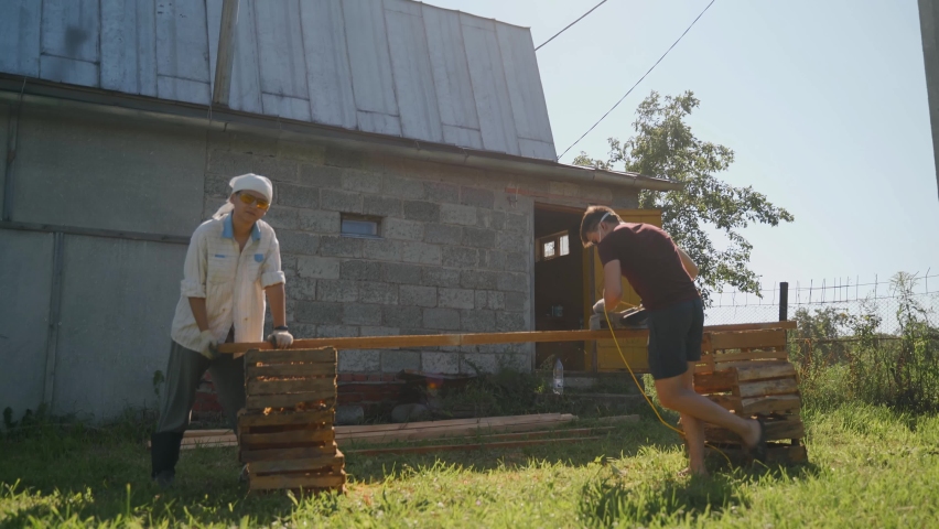 Two guys are stricter wooden bars using electric shirts. The boys are building a summer house.
