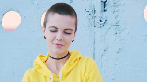 Close up of young attractive woman with shaved hair in urban outdoor city background. Portrait attractive hipster with nose piercing at summer.