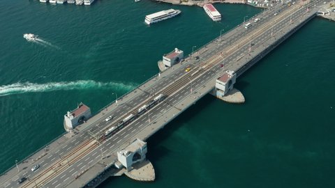 Public Transport Tram Train passing Galata Bridge over Bosphorus in Istanbul with Boats on water, Scenic Aerial low angle follow shot