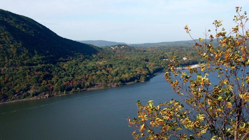 Panning view from the Breakneck Ridge hiking trail near Cold Spring, New York, in the Lower Hudson Valley. Hudson River, a cargo ship, and a freight train at the base of Storm King Mountain Royalty-Free Stock Footage #1060341632