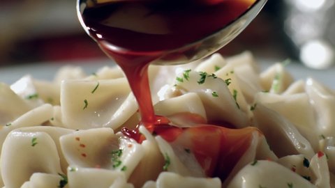 Slow motion spices and yogurt are poured over the Turkish manti on the serving plate.Close up.