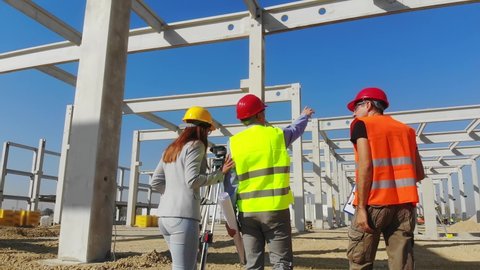 Group of builders and architect walking on construction site. Teamwork - female architect, construction engineer, manager with tablet and clipboards talking about the project, handheld shot, low angle