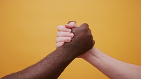 black and white hands holding together, high five shake isolated on the orange background. Close up. High quality 4k footage