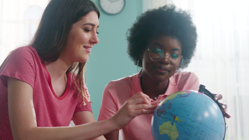 Young women, best friends, travelers, are staying home, discussing their past and future travels, use globe to share some memories, Close up, Slow motion.