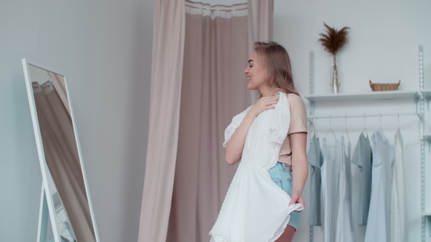 Clothes Fitting, Travel Fees, Happy Holidays, Journey Path. Cheerful woman tries on a dress at home by the mirror and throws it on the bed while collecting things for a trip Royalty-Free Stock Footage #1060347056