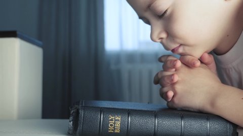 little boy praying bible. religion concept holy book bible. little boy prays at lifestyle home in the evening by the bed on the bible