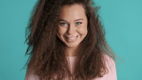 Charming bushy brunette girl cutely posing on camera isolated on blue background