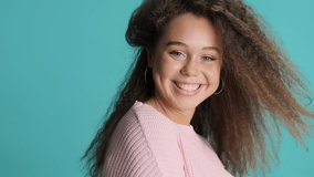 Cheerful brunette girl playing with her fluffy hair and smiling on camera over colorful background. Happy emotion