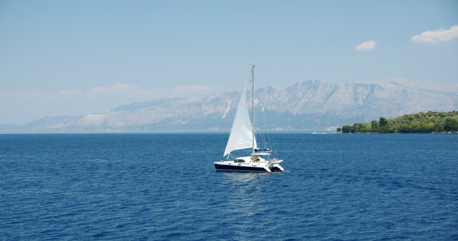 Catamaran yacht sailing in open blue sea. Coastline in bachground