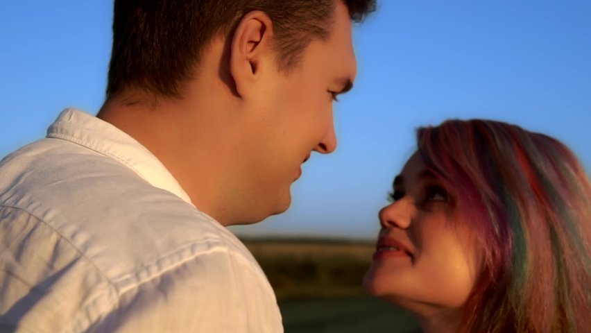 A man and a woman are talking and kissing standing in a summer field in slow motion. Young caucasian couple is smiling and looking at each other with love. Theme of happiness and tender relationship.