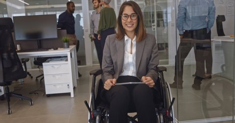 Disabled business woman in wheelchair holding table smiling in office