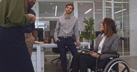 Disabled business woman in wheelchair chatting with coworkers in office