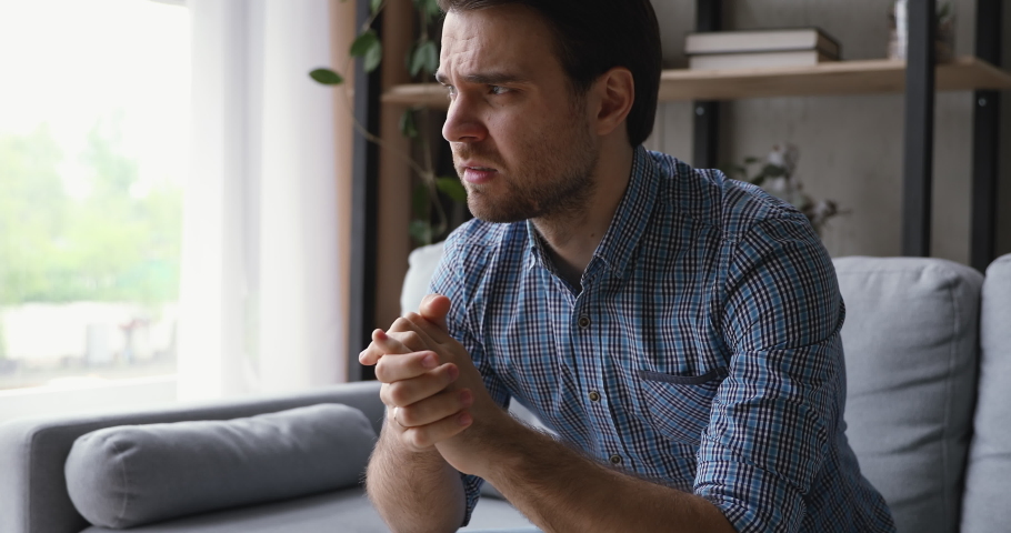 Anxious young man thinking of difficult decision, feeling doubtful. Unhappy stressed guy suffering from psychological problems, relations break up or overcoming unpleasant life moments alone at home. Royalty-Free Stock Footage #1060360700