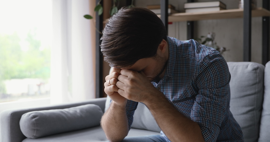 Anxious young man thinking of difficult decision, feeling doubtful. Unhappy stressed guy suffering from psychological problems, relations break up or overcoming unpleasant life moments alone at home. | Shutterstock HD Video #1060360700