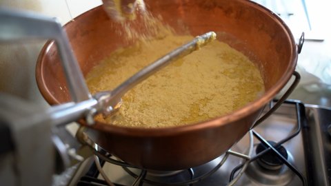 Pouring yellow corn flour in copper cauldron with boiling water, natural healthy harvest perfect for traditional winter dishes preparation. Cooking maize porriage called polenta