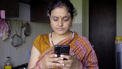indian women using mobile in kitchen getting inspired disappoint