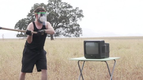 Male smashing the screen of an old television with pickaxe to relieve stress