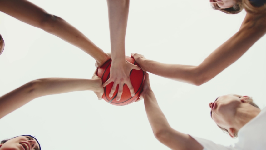Close-up of five women players holding basketball ball in star standing in circle together agaoinst white sky background. Team spirit. Professional sports team. | Shutterstock HD Video #1060373930