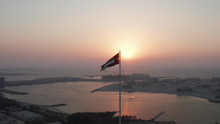 Flag of United Arab Emirates waving in the wind with sun setting behind during sunset in Dubai; silhouette video of UAE flag Royalty-Free Stock Footage #1060374458