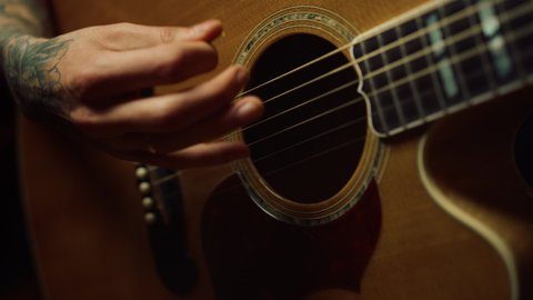 Closeup man fingers holding mediator in recording studio. Man hand playing guitar in dark room. Unrecognizable person rehearsing with acoustic guitar in recording studio.