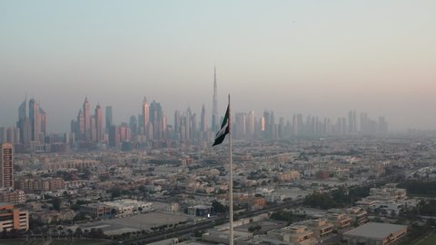 Flag of UAE, United Arab Emirates waving in the wind with Burj Khalifa and Dubai skyline in background during sunset
