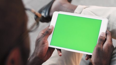 Young African American man looking at tablet with green screen. Chroma key on tablet screen. Back view.