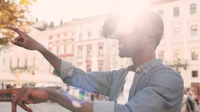 Handsome African American man playing in virtual reality headset on sunlight on street. Young guy takes off his VR glasses and looks around.