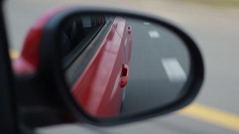 Video shooting in motion, view in the rear view side mirror of a car, driving a red car along the road